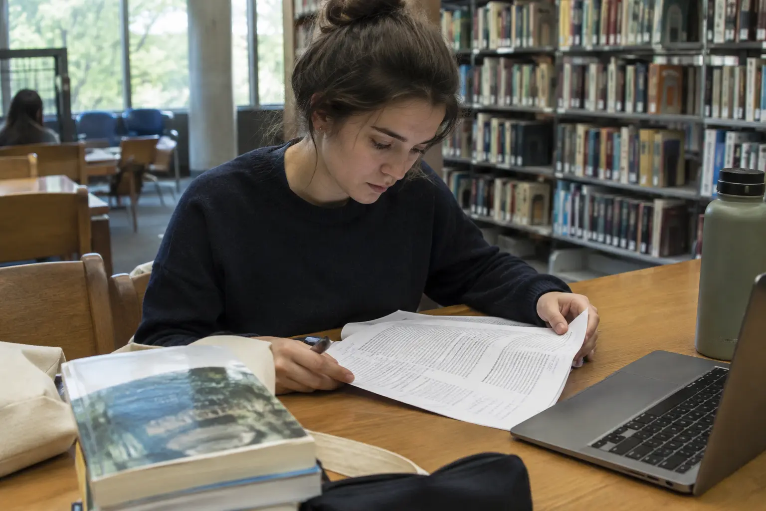 Estudiante de Turismo leyendo un artículo académico impreso con notas al margen en una biblioteca