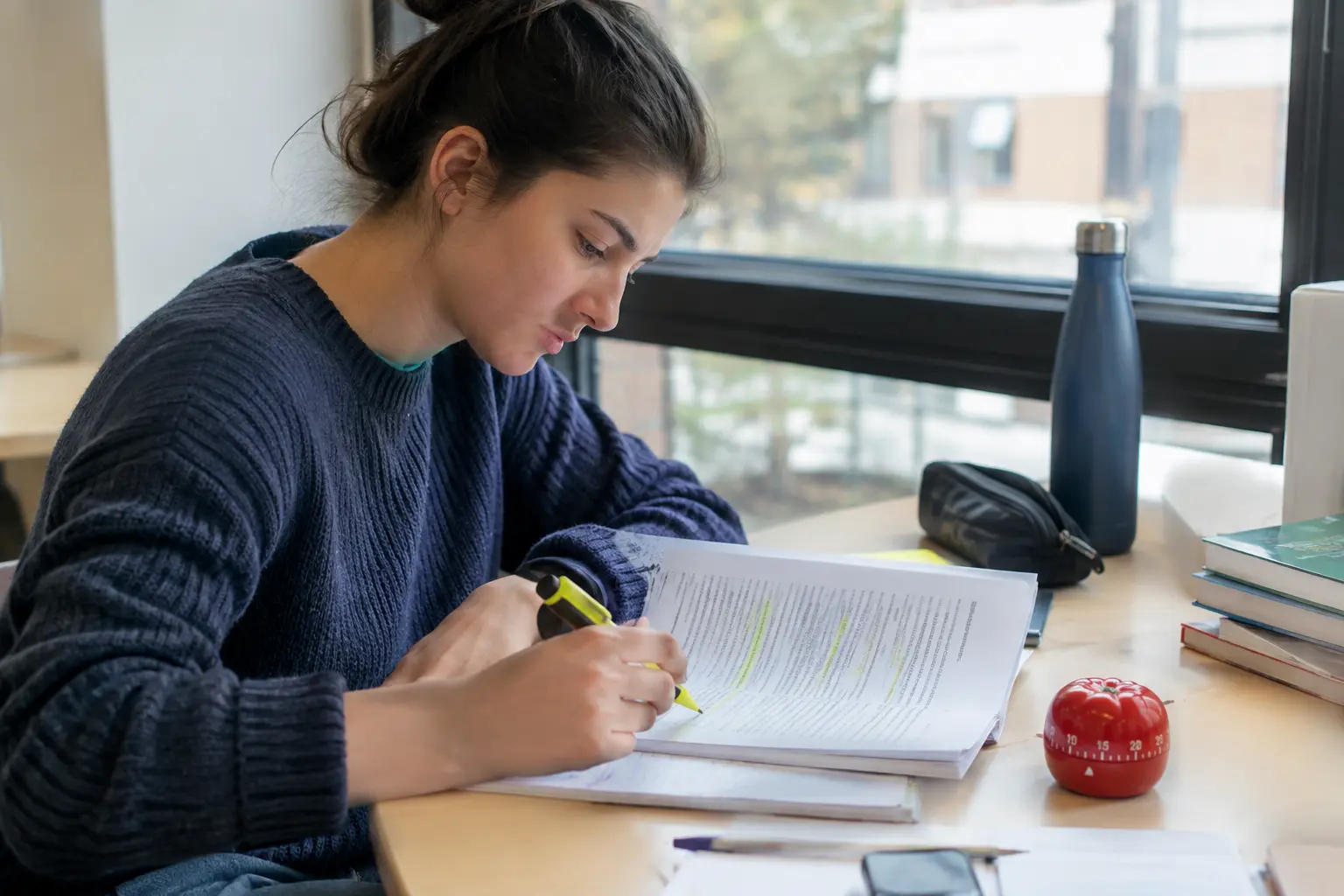 Estudiante leyendo una tesina con un cronómetro sobre el escritorio para organizar su hora de lectura